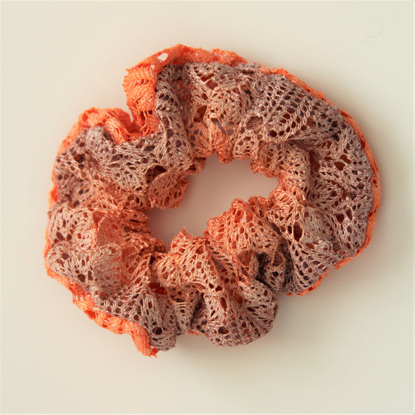 Lace hair scrunchie in gradiated colours from coral to lilac on a white surface