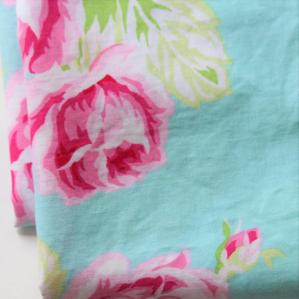 A folded piece of fabric with large-scale pink peonies on an aqua background