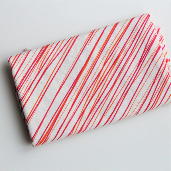 A folded piece of white fabric with an orange and bright pink sketchy stripe pattern lies on a white background.