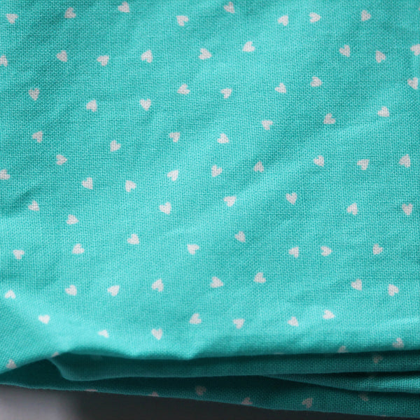 A folded piece of turquoise fabric with tiny white hearts