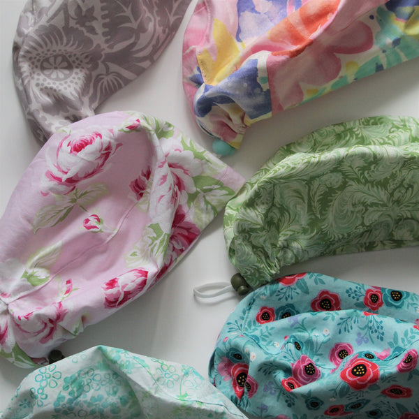 A selection of colourful handmade scrub hats in floral and abstract patterns lie on a white background.